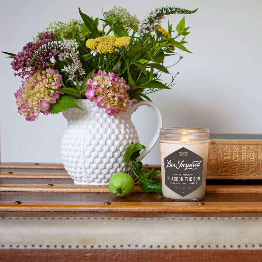 a Place in the Sun jelly jar candle burning next to a vase of flowers