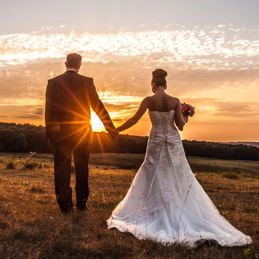 groom and bride holding hands in a field at sunset