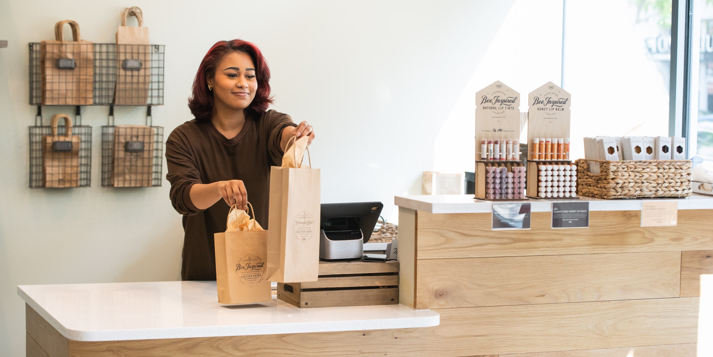 worker holding out shop bags from behind the counter at bee inspired honey retail store