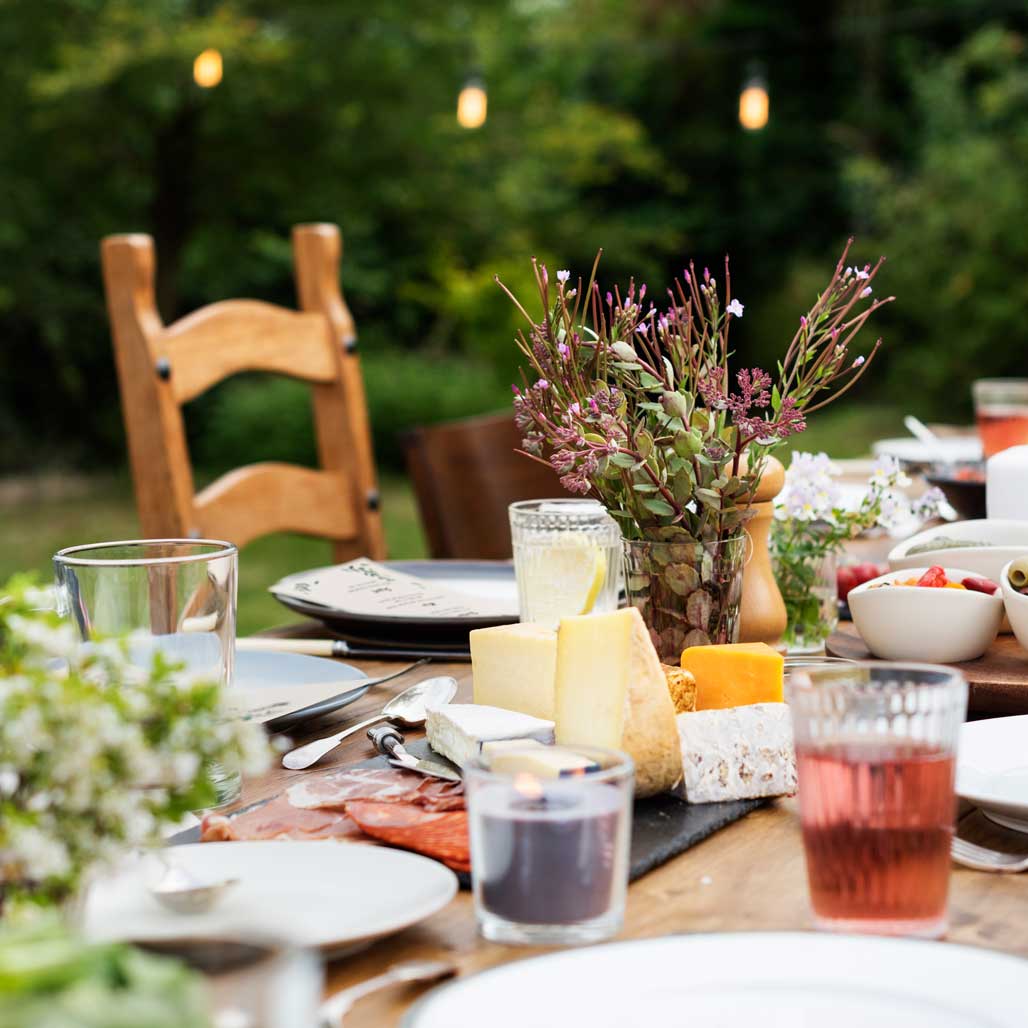 An outdoor table set up with cutlery, floral centerpieces, and assorted cheese