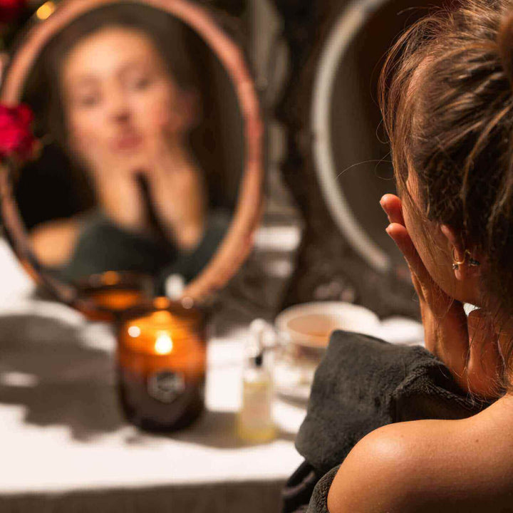 Woman does skincare in front of a candle and a mirror