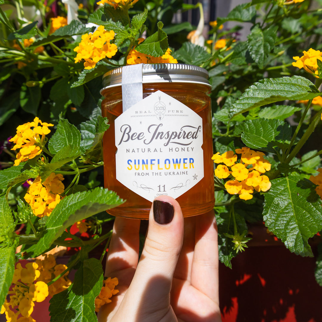 holding jar of Ukrainian Sunflower honey in front of flowers