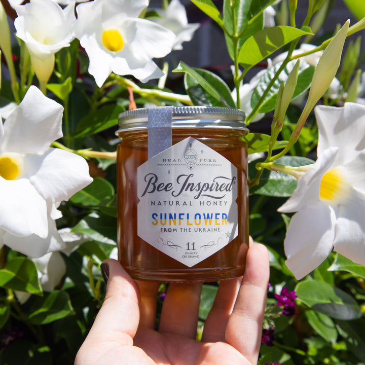 holding jar of Ukrainian Sunflower honey in front of white flowers