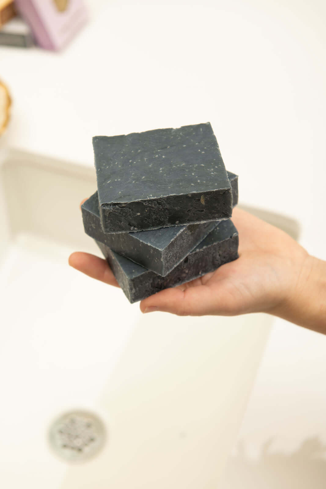 Person holding black clay bar soap stack over the sink