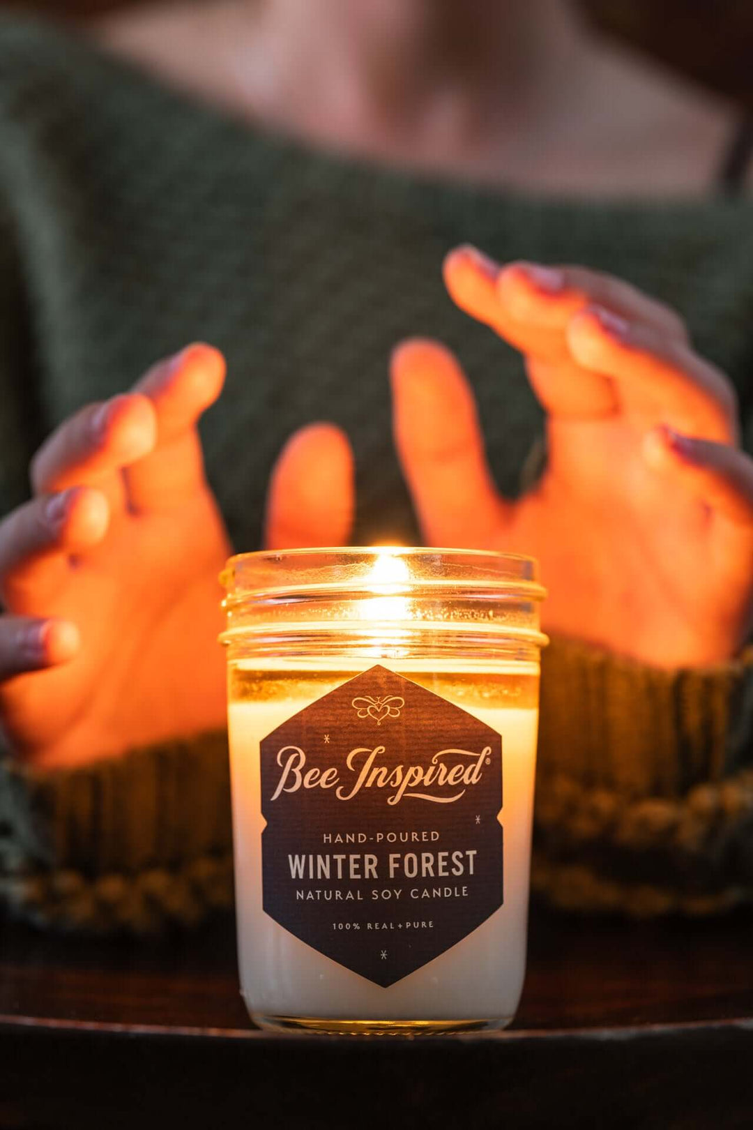 Person warming hands over flame of Winter Forest jelly jar candle