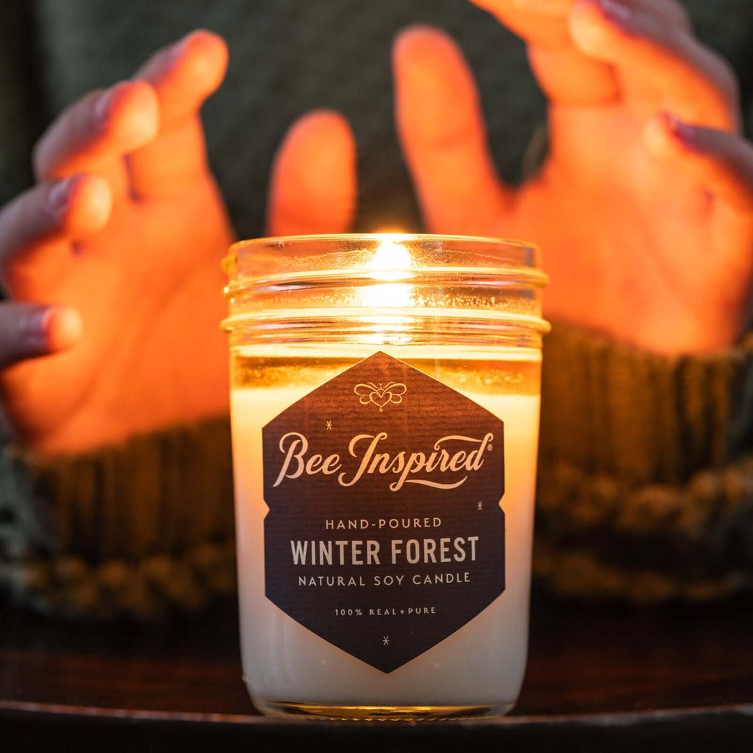 Person warming hands over flame of Winter Forest jelly jar candle