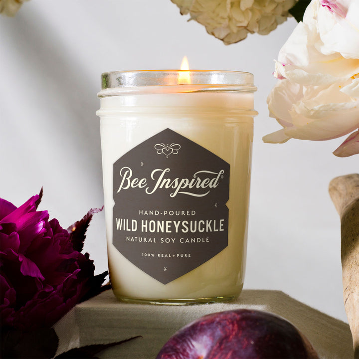 Wild Honeysuckle jelly jar burning next to white and purple flowers