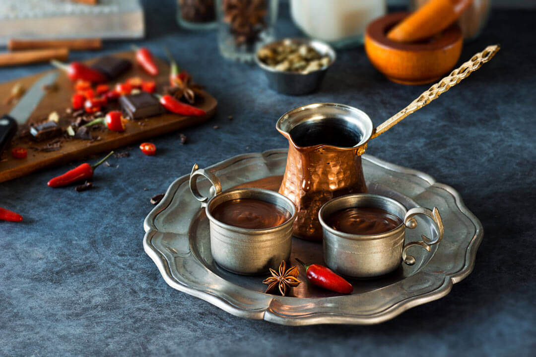 two mugs of Mexican hot chocolate on a silver serving tray with a hot pepper