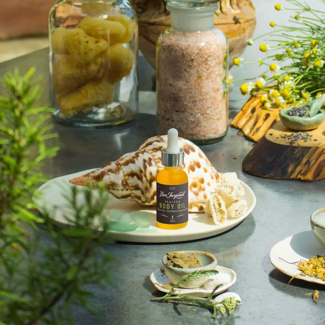 Se+Tea body oil on a table decorated with shells, driftwood, flowers, and sea glass