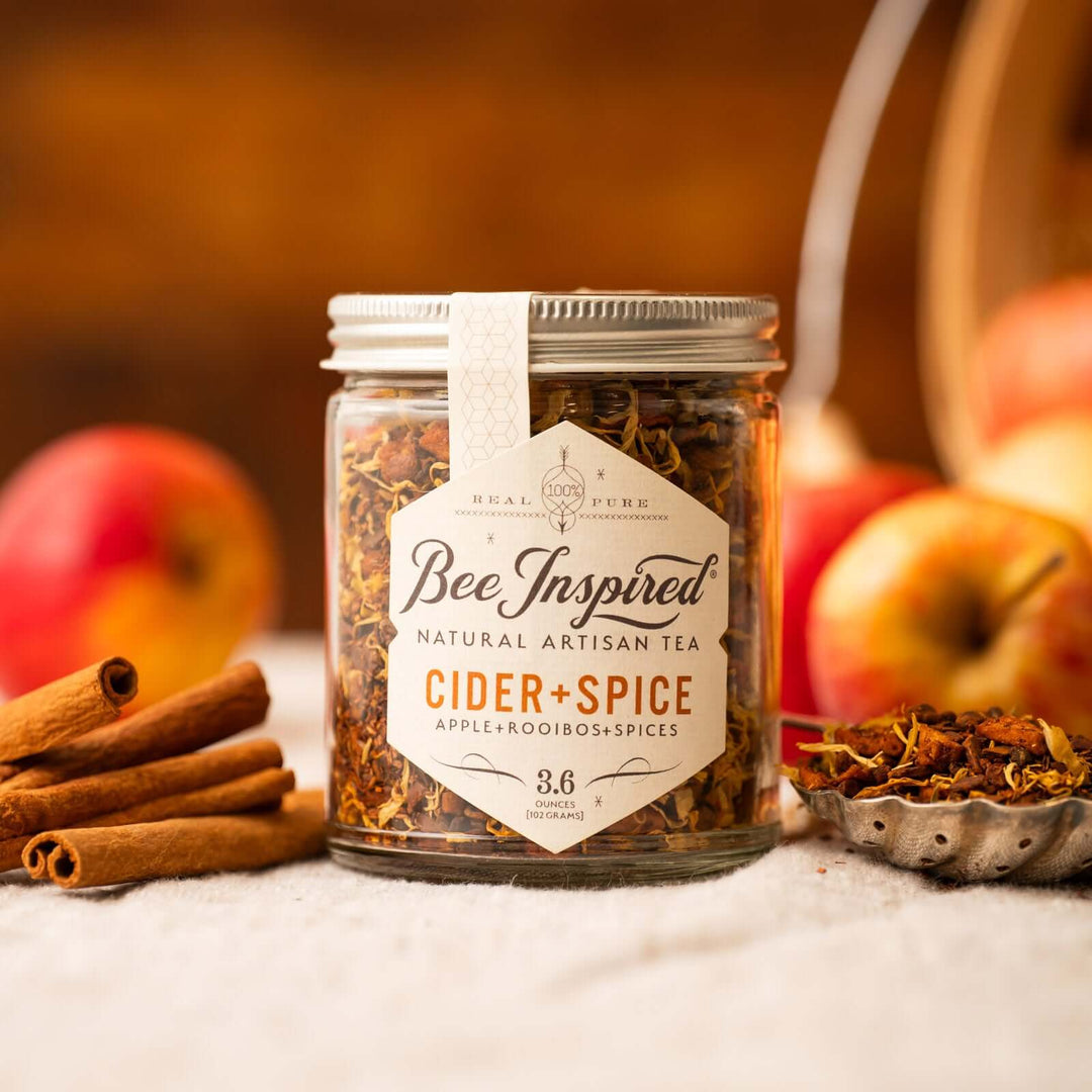 Bee Inspired Cider+ Spice tea next to fresh apples and cinnamon sticks