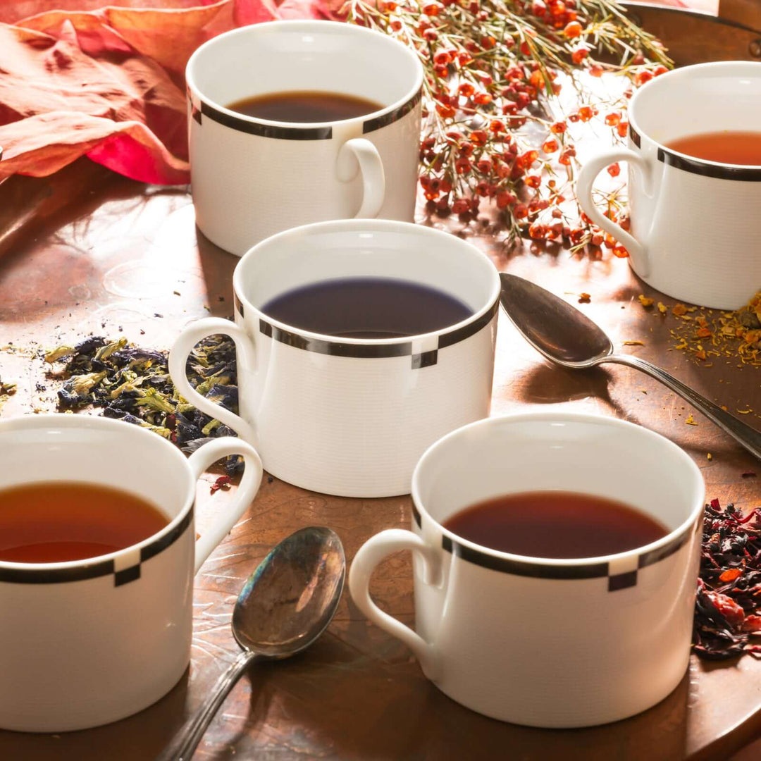 five cups of bee inspired tea with spoons with loose leaf tea spread around