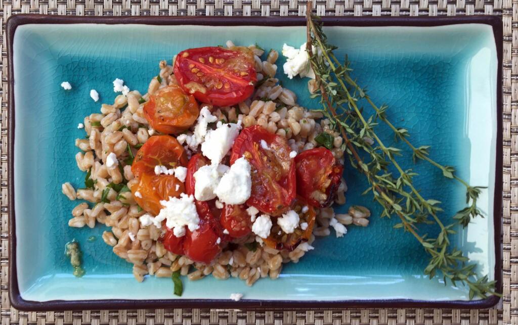 roasted cherry tomatoes on top of farro salad with garnish on blue plate