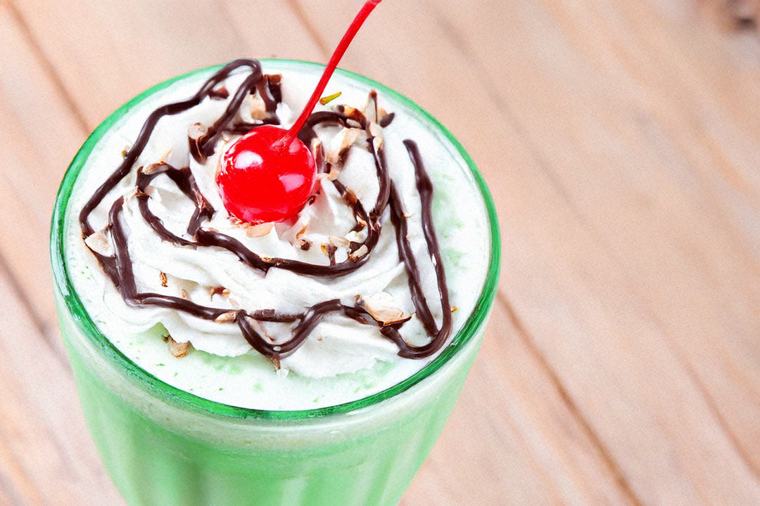 homemade shamrock shake with whipped cream, chocolate drizzle, and a cherry on top