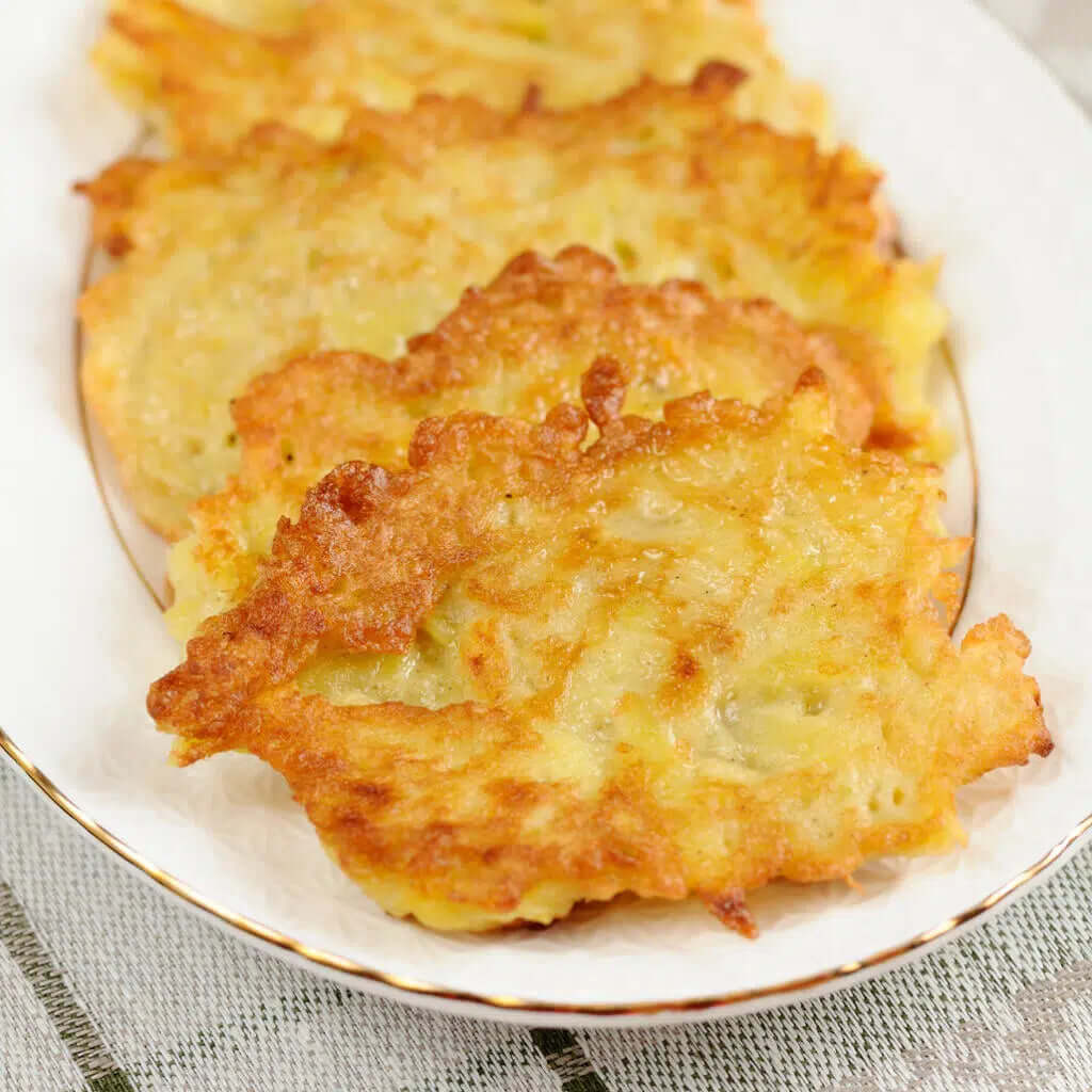 Stack of crispy golden-brown potato latkes on white plate ready to serve with applesauce