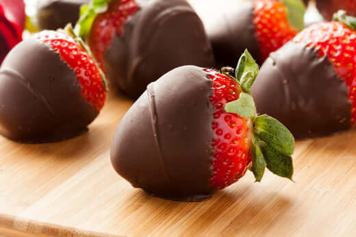 Chocolate covered strawberry being dipped in melted chocolate for Valentine's Day dessert