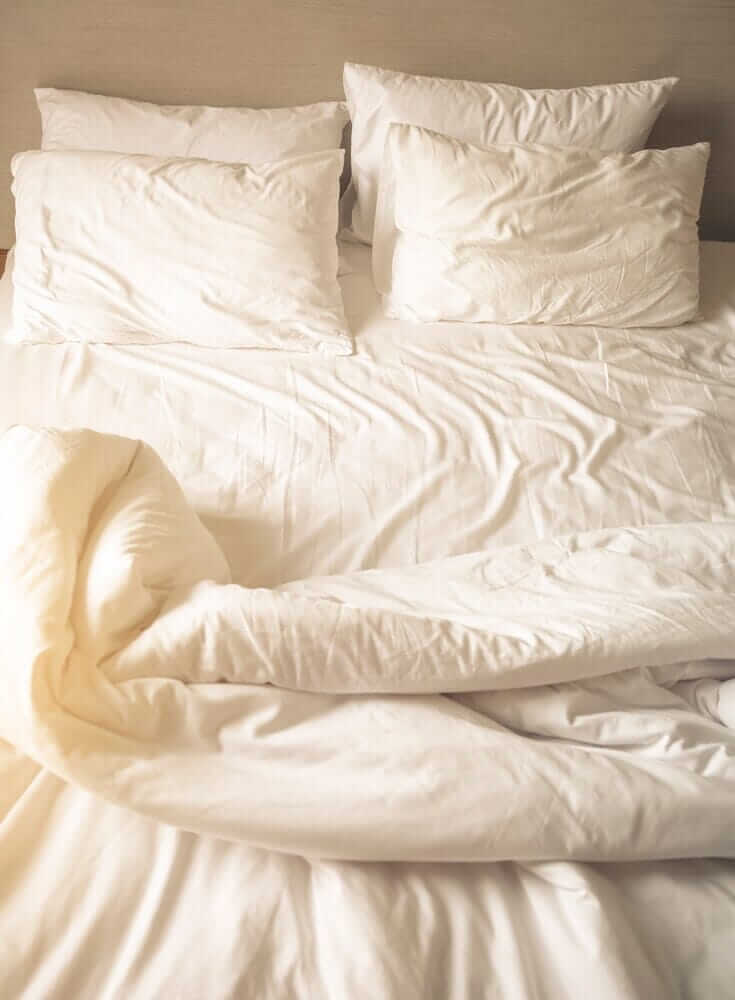 a soft, sunshine-lit unmade bed