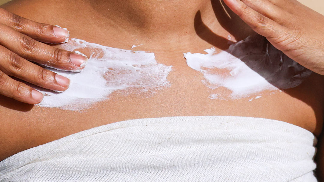 a woman spreading moisturizer on upper chest