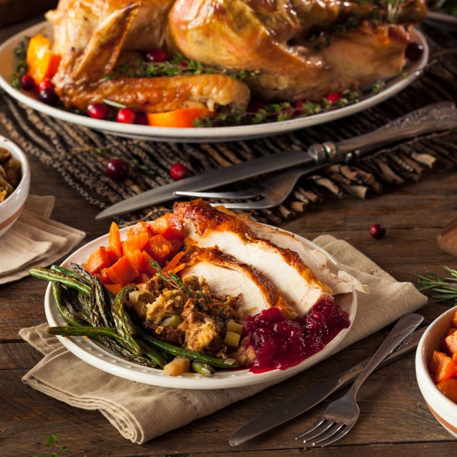 A place setting for thanksgiving. The plate has chicken, squash, cranberry relish, stuffing, and green beans.