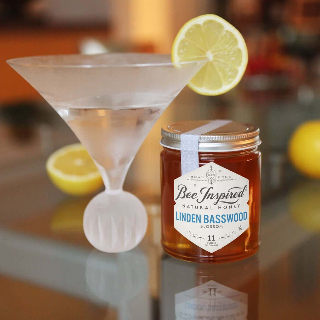 a martini garnished with lemon next to a jar of linden basswood honey