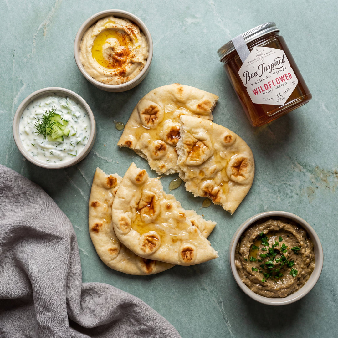 Honey naan bread with dips and a jar of wildflower honey on a textured surface