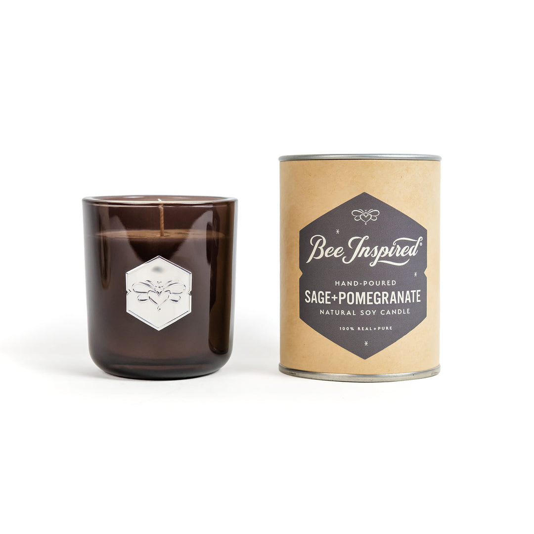 Brown candle in a glass jar with a cylindrical cardboard packaging labeled 'Bee Inspired' on a white background.