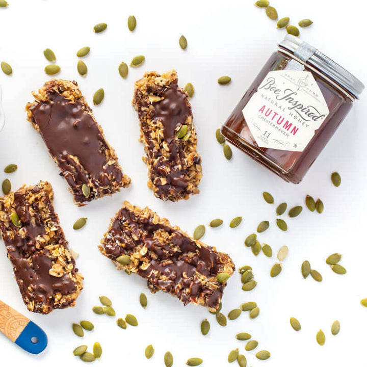 granola bars topped with chocolate next to a bowl of oats and a jar of autumn honey from bee inspired honey retail store in owings mills