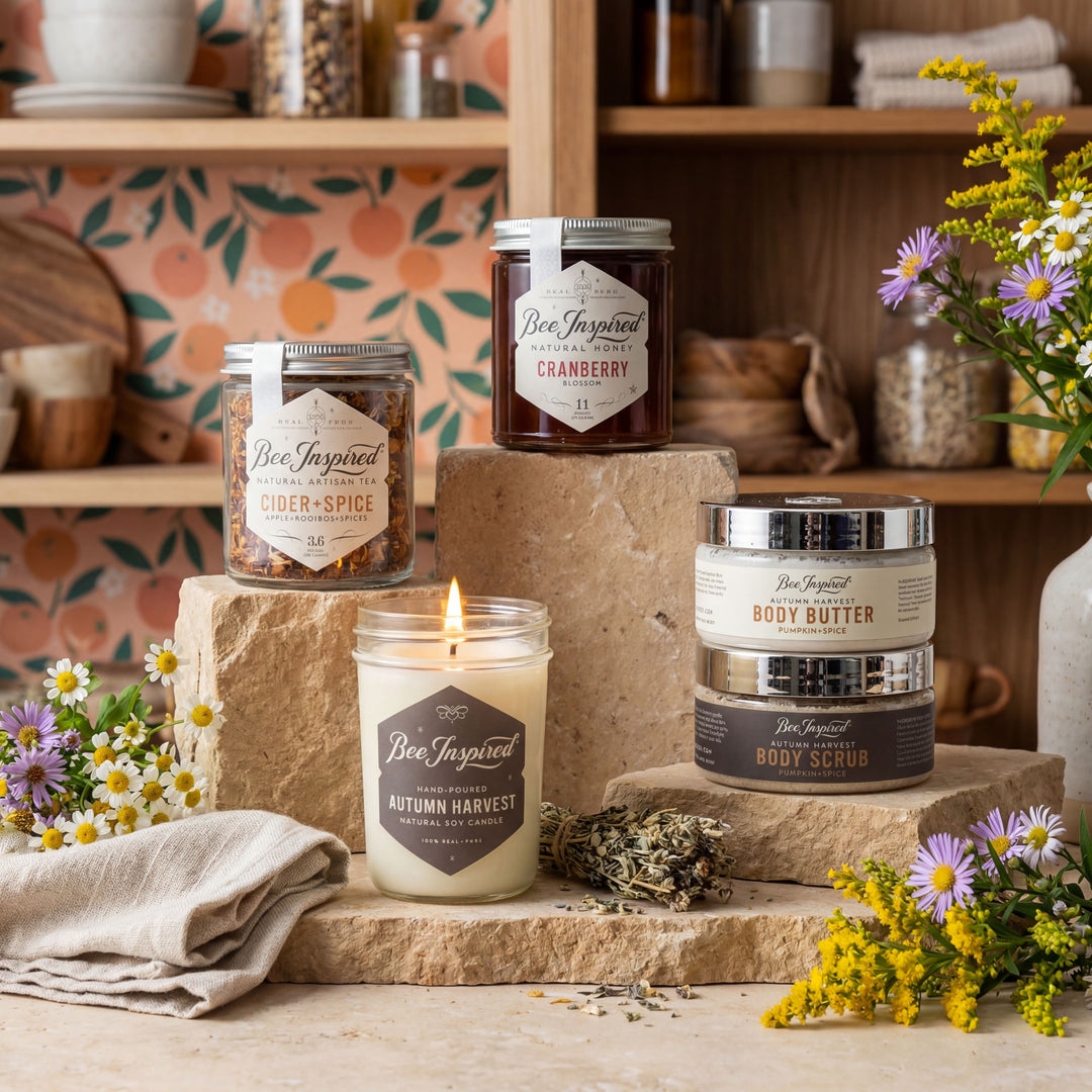 Collection of 'Bee Inspired' products including candles and body butters on a rustic surface with flowers and shelves in the background.