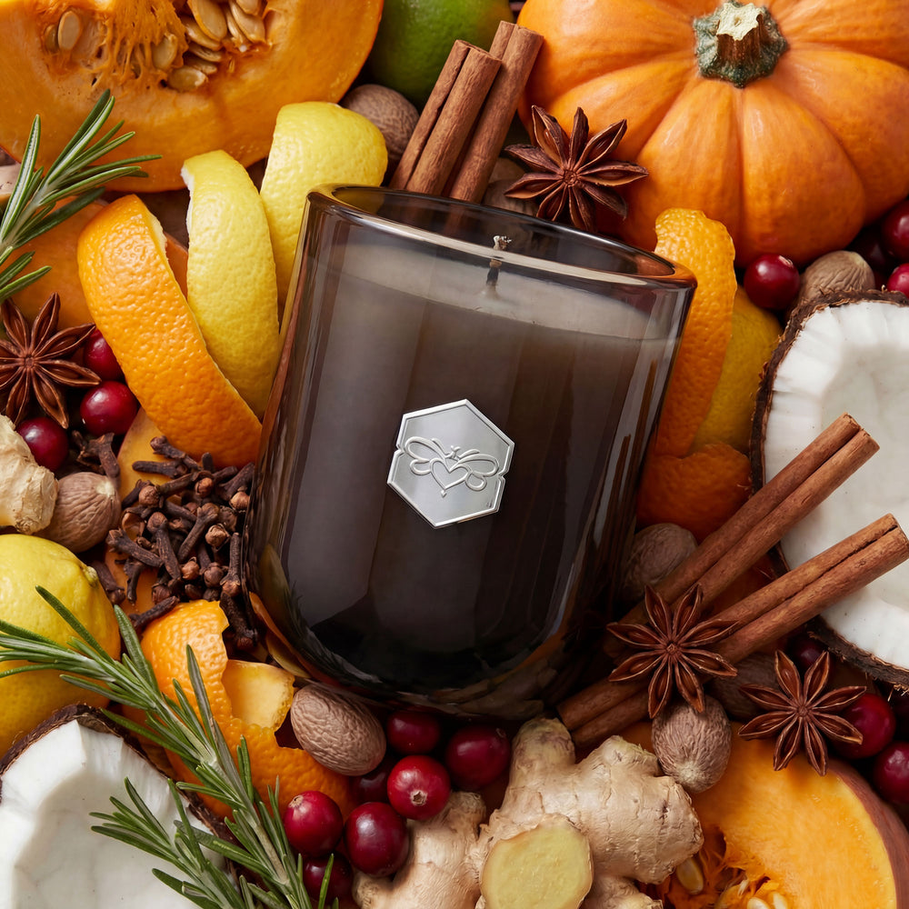 Candle surrounded by autumnal fruits and spices including oranges, apples, and nuts.
