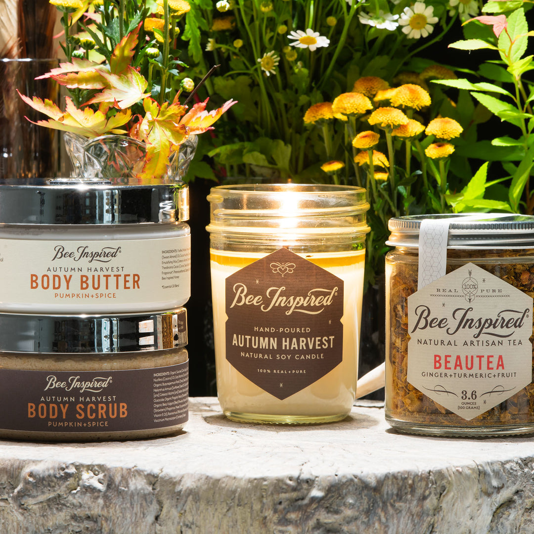 Autumn Harvest scrub and butter duo, Autumn Harvest jelly jar candle, and Beautea in front of yellow and white flowers 