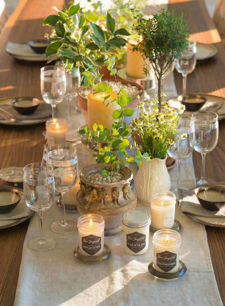 Decorative table setting with candles, plants, and glasses on a wooden table.