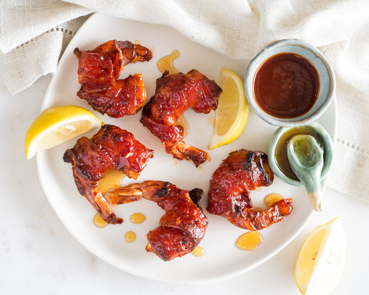 bacon-wrapped shrimp on a plate with lemon wedges and two small sauce bowls