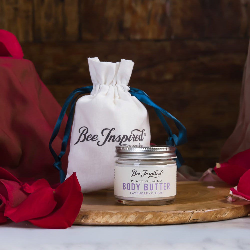 Bee Inspired body butter jar with a drawstring bag on a wooden board with red flowers.