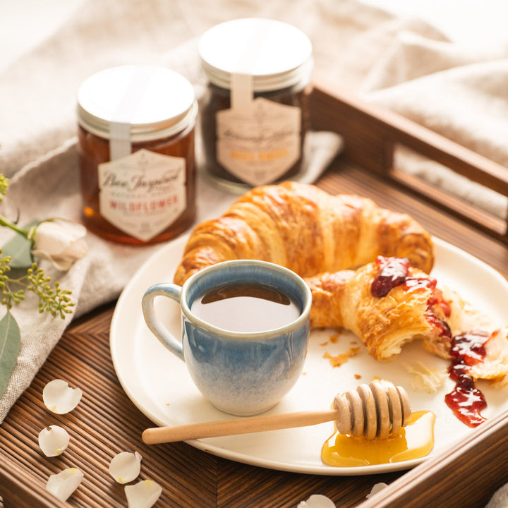 Breakfast tray with coffee, croissant, and jars on a wooden surface