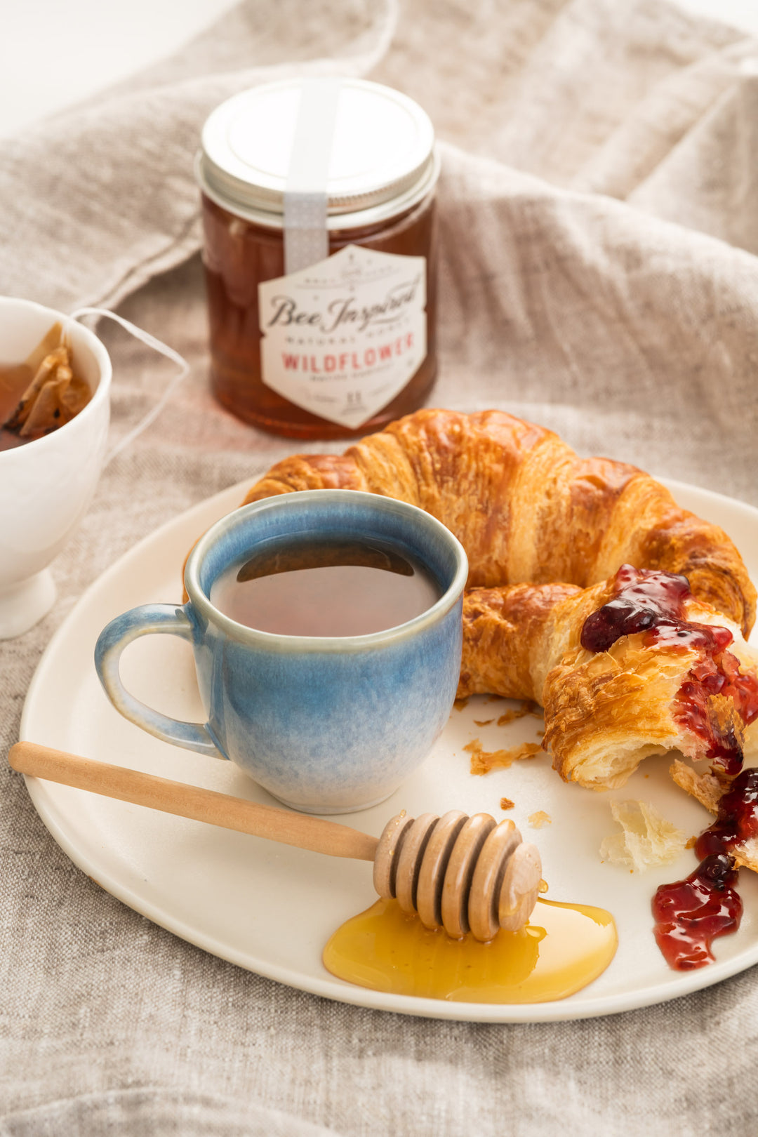 Breakfast setting with a croissant, coffee, and jar of honey on a textured surface.