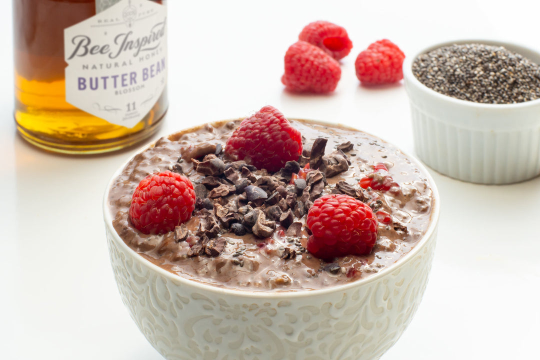 a bowl of chocolate raspberry pudding with butter bean honey from bee inspired honey retail store in owings mills, a bowl of chia seeds, and raspberries in the background