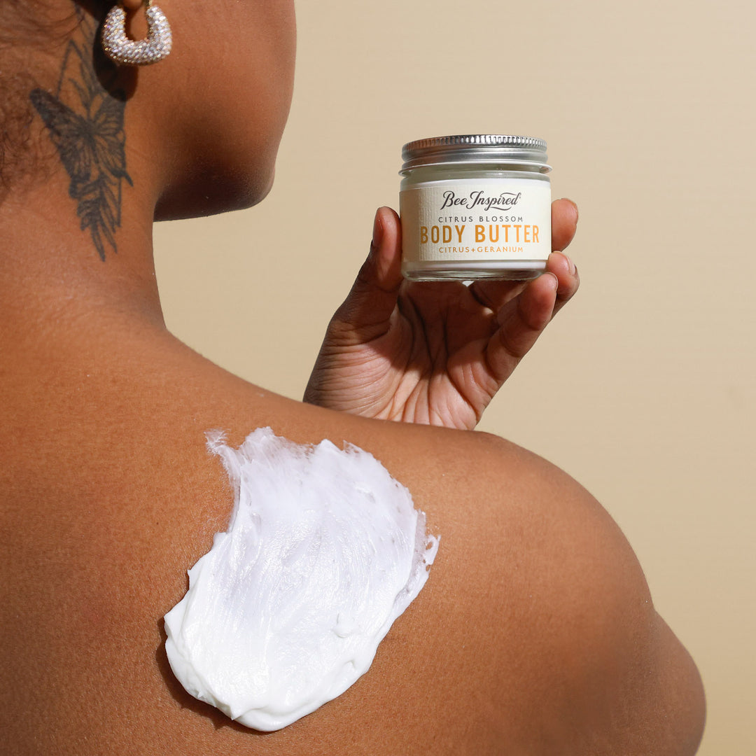 Person applying body butter to their shoulder with a jar labeled 'Body Butter' in the foreground.