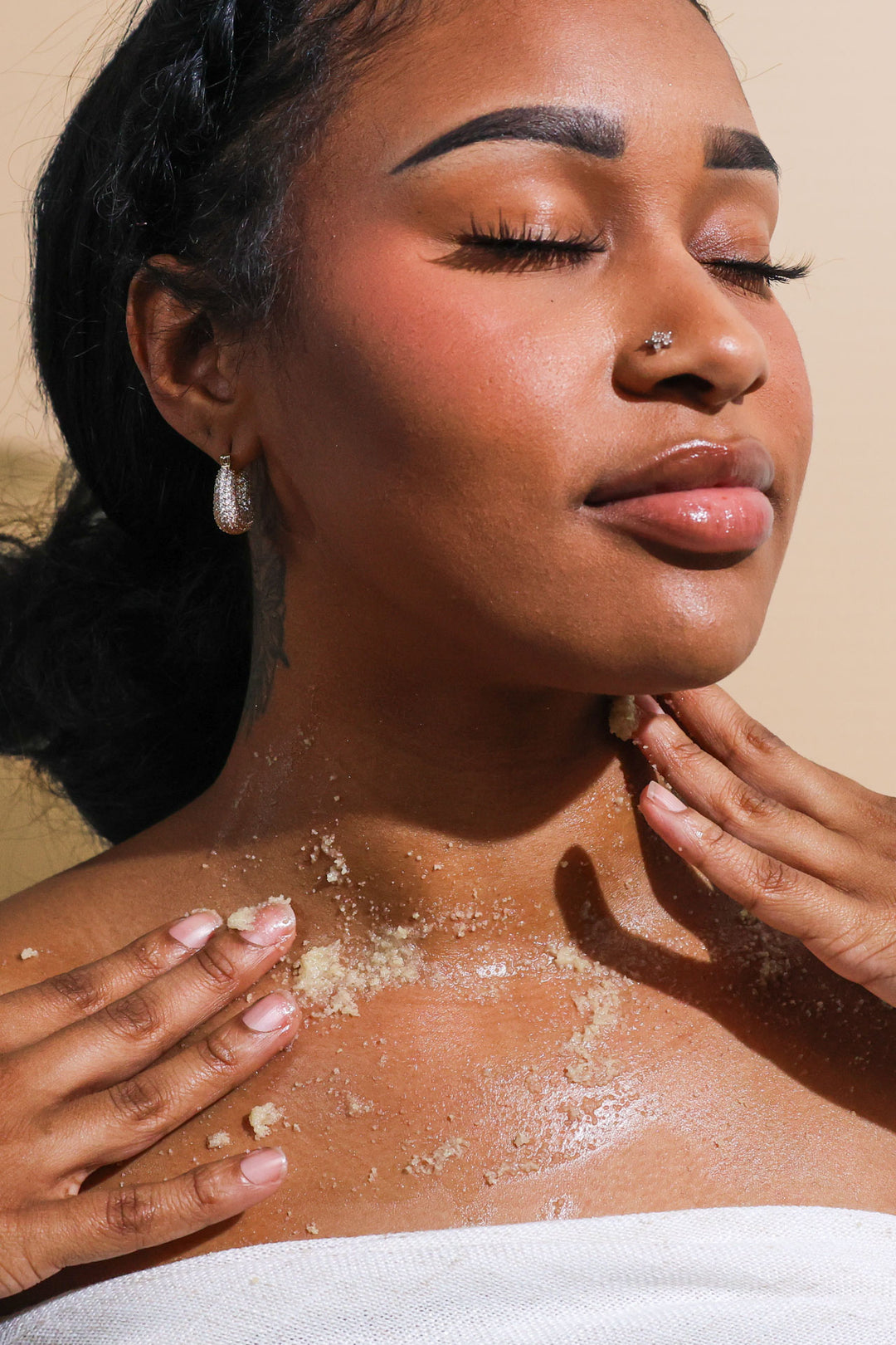 A woman using Citrus Blossom body scrub on her shoulders and chest