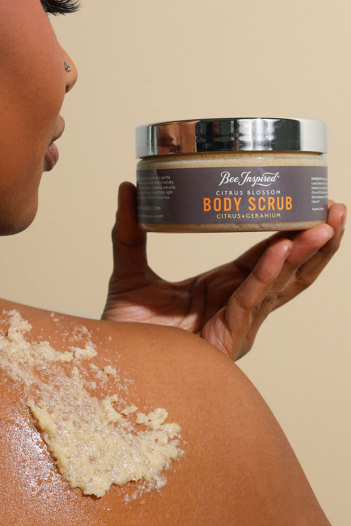 A woman using Citrus Blossom body scrub on her shoulder