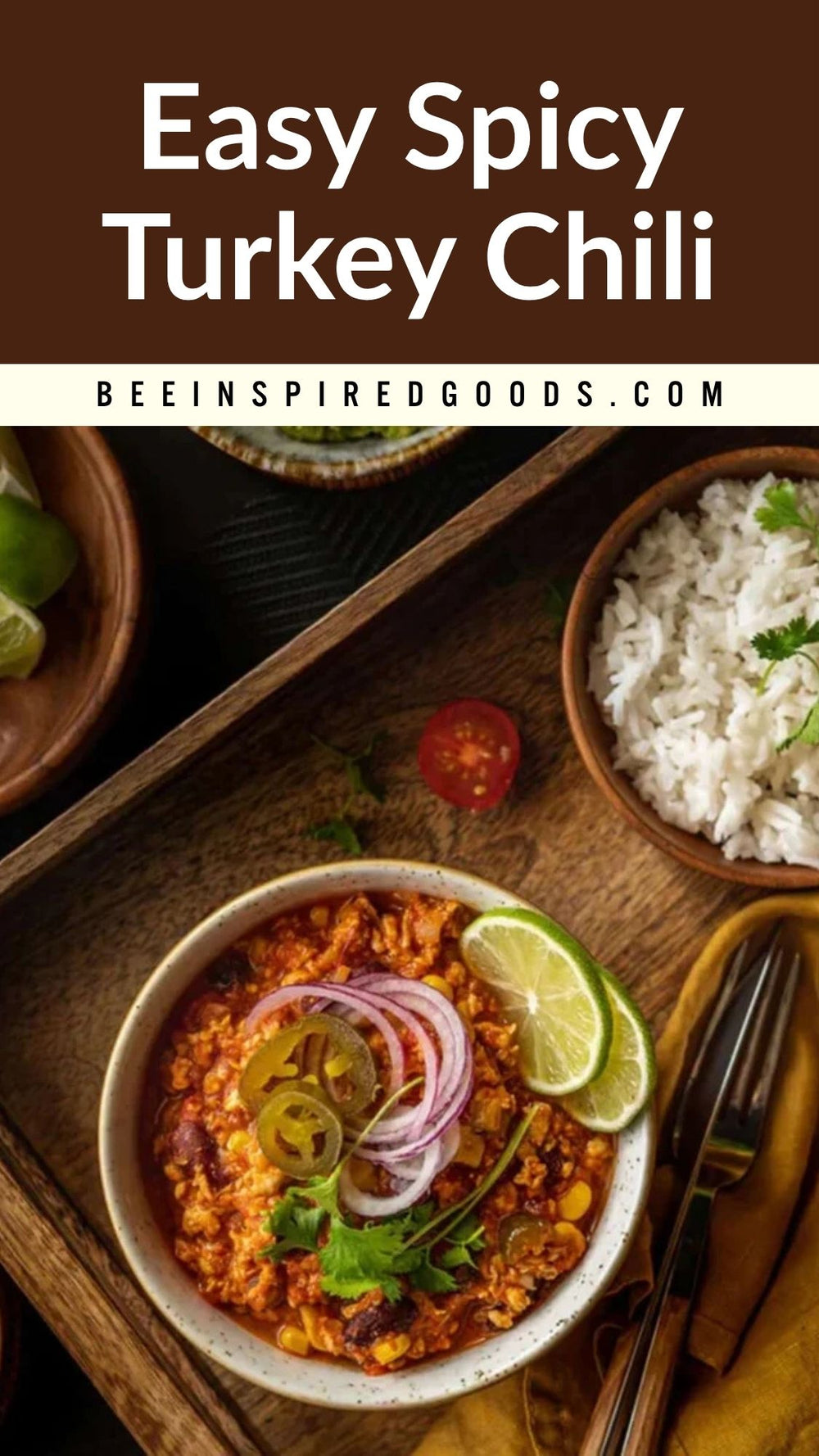 A bowl of Easy Spicy Turkey Chili topped with red onion, lime slices, and jalapeño slices, served on a wooden tray with white rice and a fork. The image includes a text banner at the top reading 'Easy Spicy Turkey Chili' and 'BEEINSPIREDGOODS.