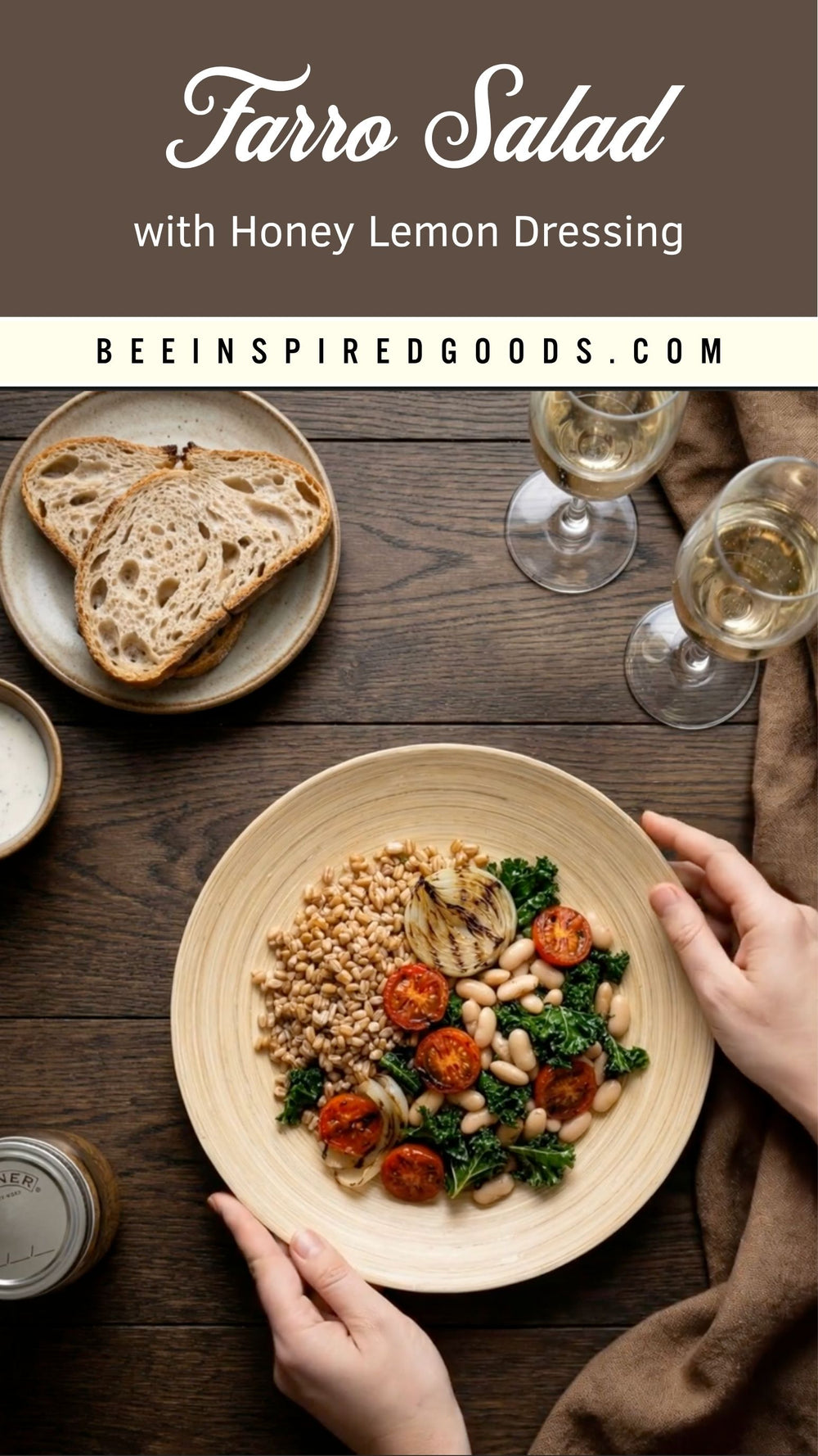 A top-down view of a plated Farro Salad with Honey Lemon Dressing on a dark wooden table, with hands holding the plate, slices of bread on a side plate, wine glasses, and a brown cloth. Text at the top reads 'Farro Salad with Honey Lemon Dressing' and 'BEEINSPIREDGOODS.