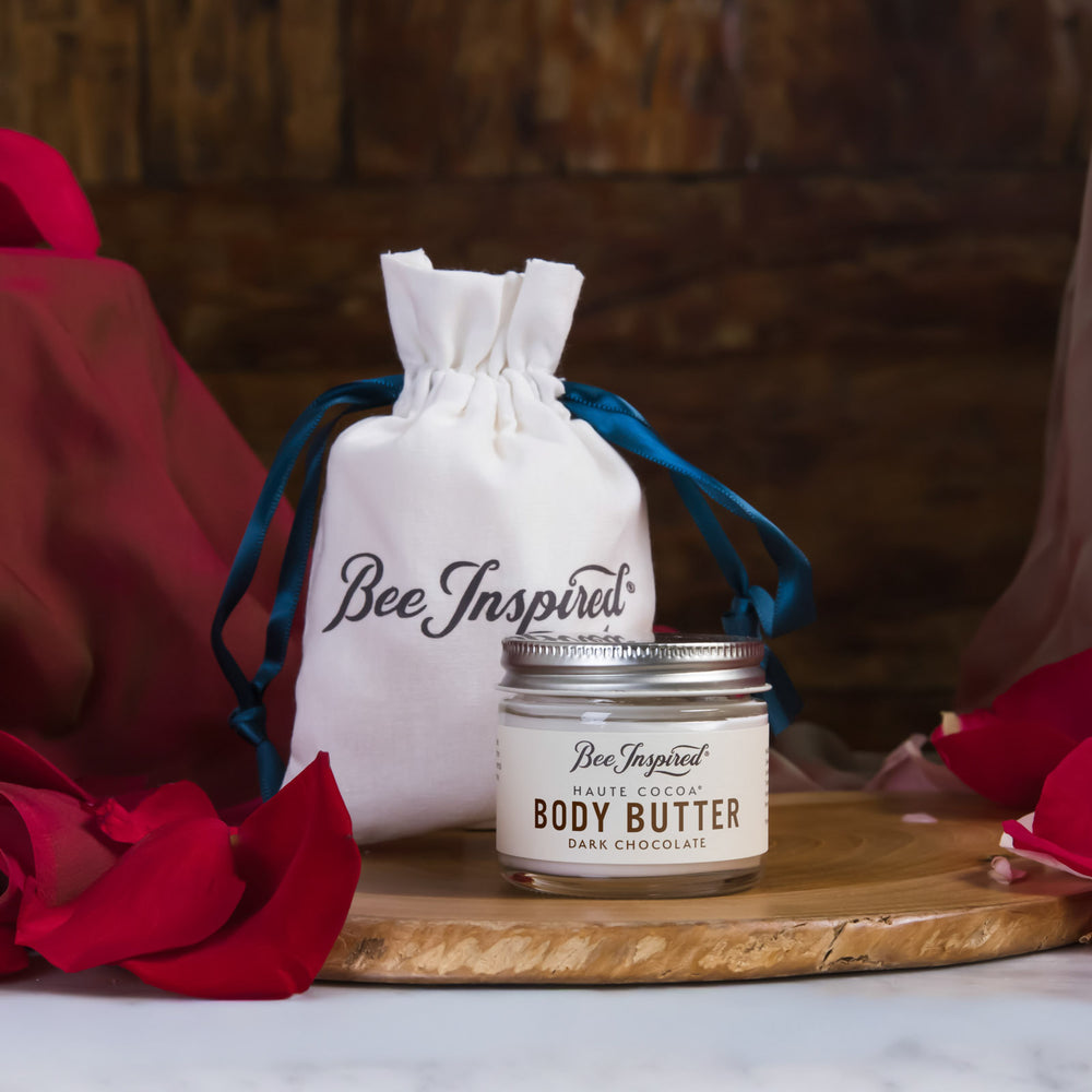 Body butter jar with a drawstring bag labeled 'Bee Inspired' on a wooden board.