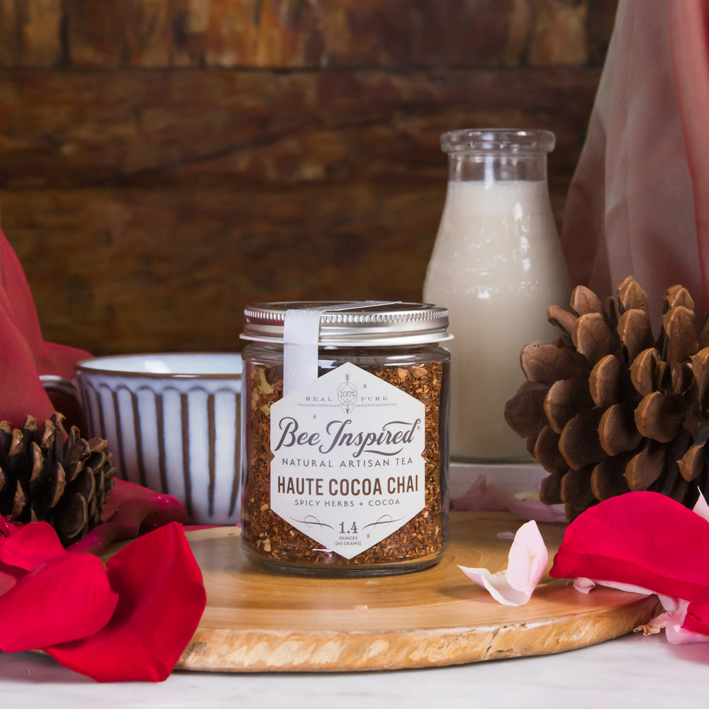 Jar of 'Bee Inspired' haute cocoa chai on a wooden board with a bottle of milk and decorative elements.