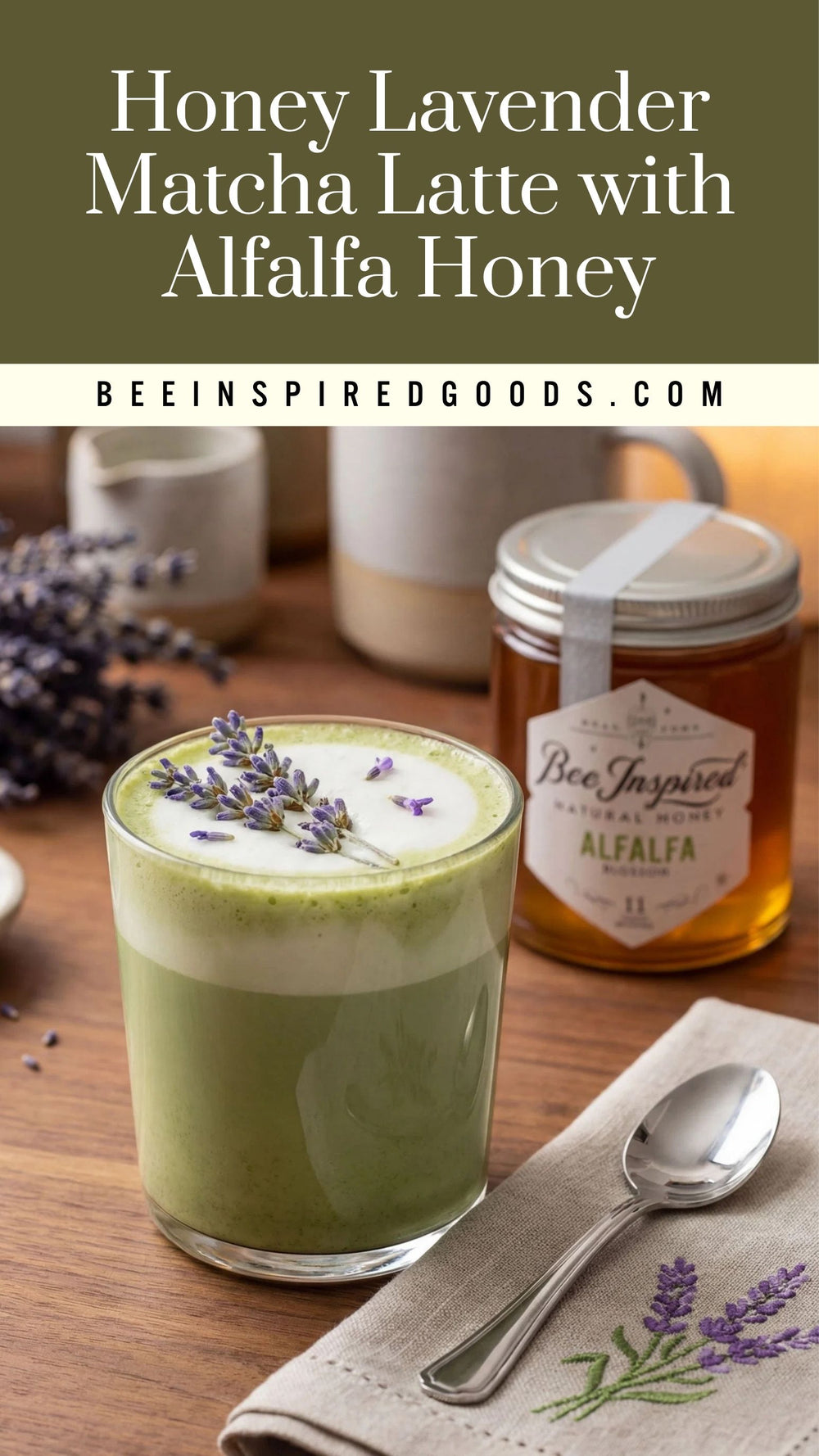A glass of layered honey lavender matcha latte topped with lavender sprigs, shown on a wooden table with a jar of alfalfa honey, a spoon, and a napkin. Text at the top reads 'Honey Lavender Matcha Latte with Alfalfa Honey' and 'BEEINSPIREDGOODS.