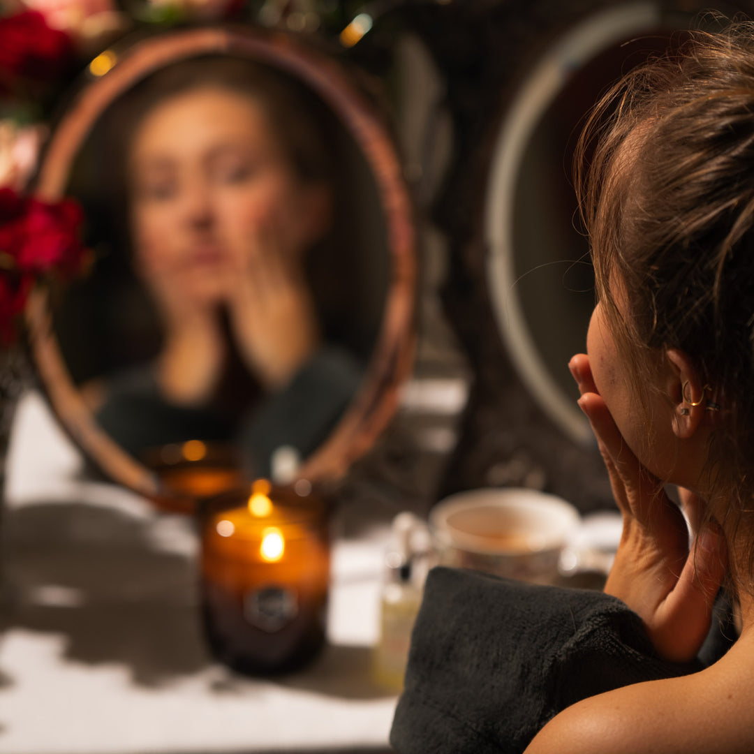 woman looking at her face in a mirror with a luxe candle on the tabel