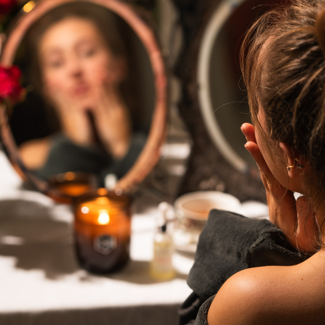 Woman does skincare in front of a candle and a mirror 