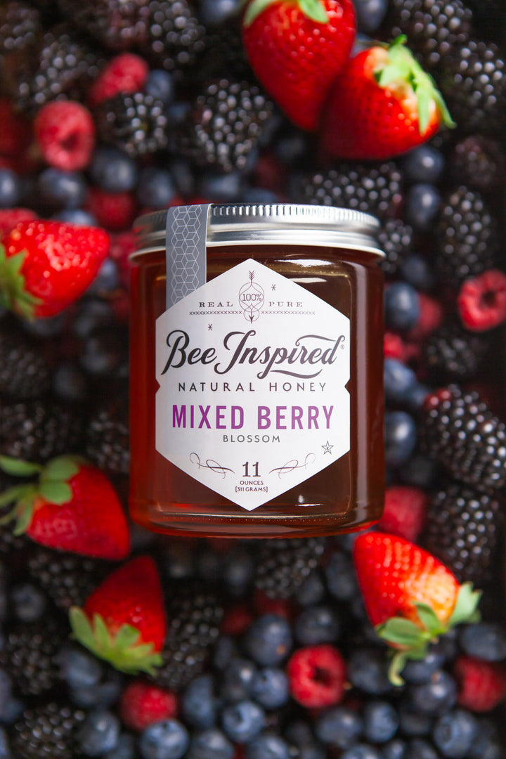 a jar of mixed berry honey lfrom bee inspired honey retail store in owings mills aying on a bed of blackberries, blueberries, raspberries, and strawberries