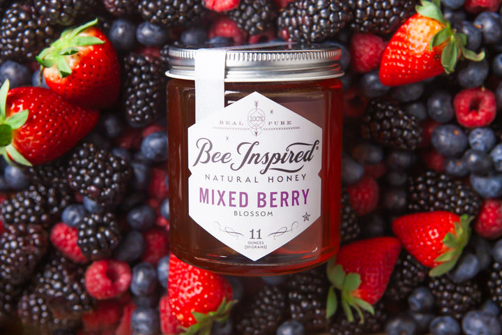 a jar of mixed berry honey lfrom bee inspired honey retail store in owings mills aying on a bed of blackberries, blueberries, raspberries, and strawberries