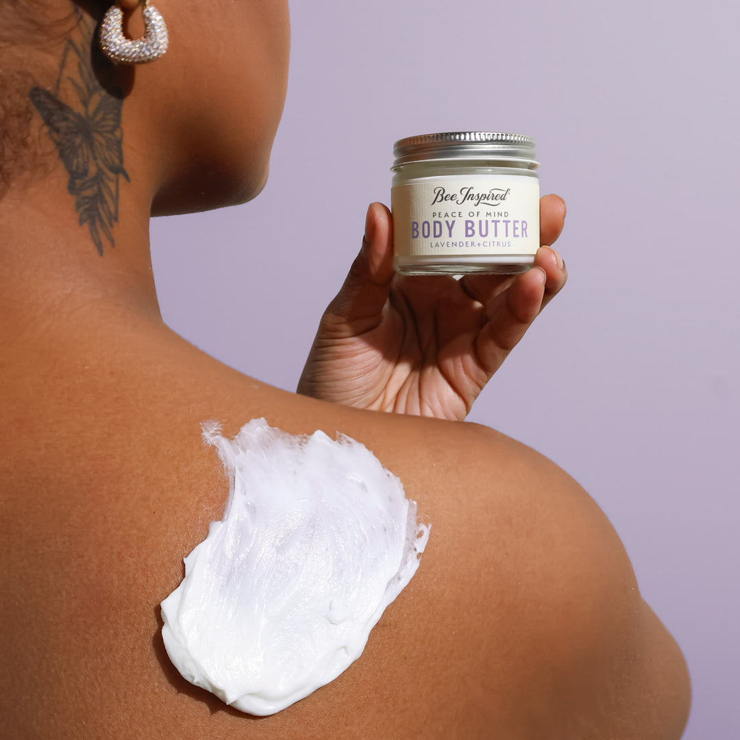 Person applying body butter to their shoulder with a jar labeled 'Body Butter' in the foreground.