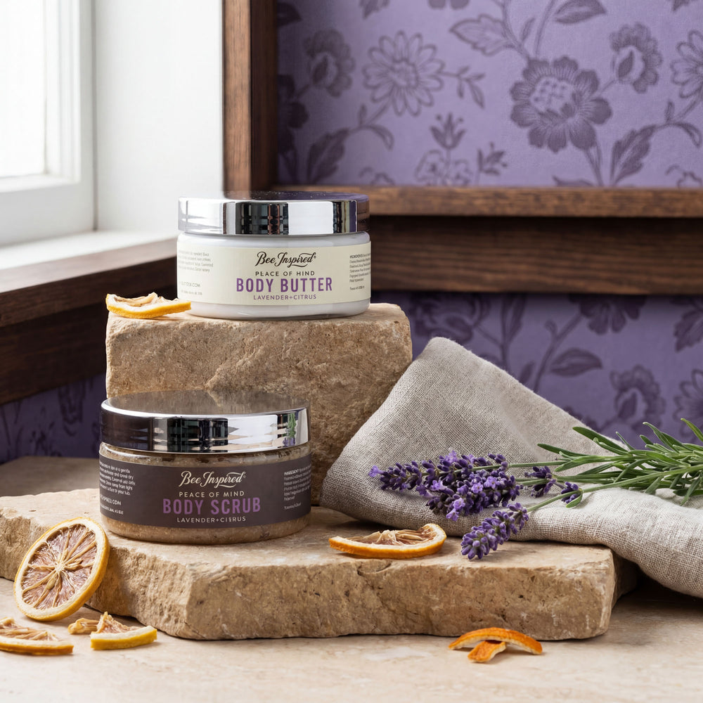 Two jars of body products on a wooden surface with lavender and orange slices, against a floral wallpaper background.