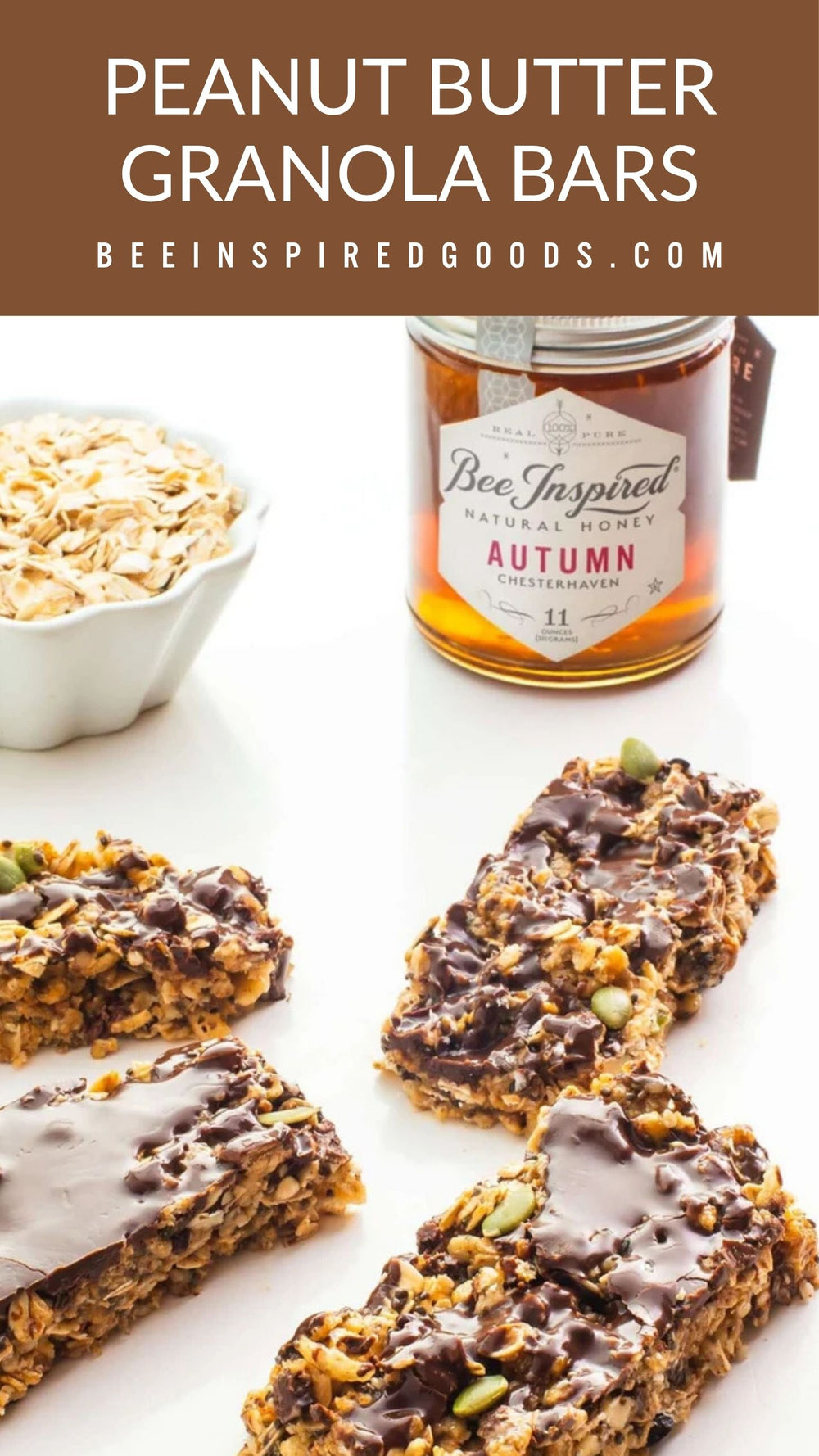 Four peanut butter granola bars topped with chocolate and pumpkin seeds are arranged on a white surface, with a bowl of oats and a jar of Bee Inspired Honey Autumn flavor in the background. A brown banner at the top reads 'PEANUT BUTTER GRANOLA BARS' and 'BEEINSPIREDGOODS.